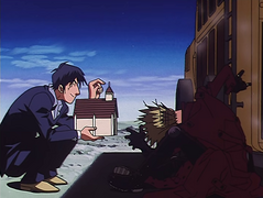 Wolfwood indicates where to insert a coin, urging Vash to give it a try.